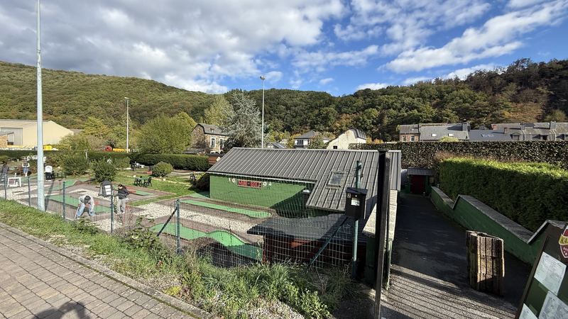 Le parcours du mini-golf et son bâtiment vert, avec les collines boisées de La Roche-en-Ardenne en arrière-plan